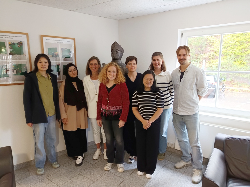 Gruppenfoto der CuKnow-Mitglieder in einem hellen Raum mit Fenstern und Ritterrüstung im Hintergrund.