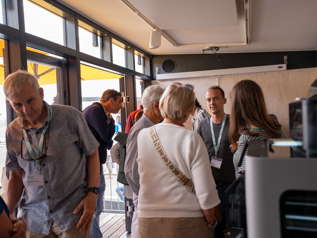 Einige Menschen schauen sich im MobiLab um. An der Seite steht ein 3D-Drucker.